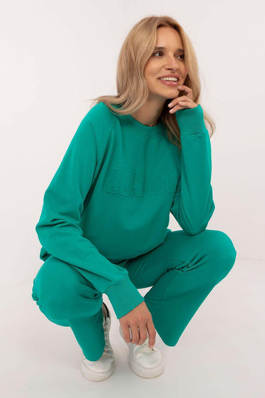 Green crewneck sweatshirt and jogger pants set, model crouching with long sleeves