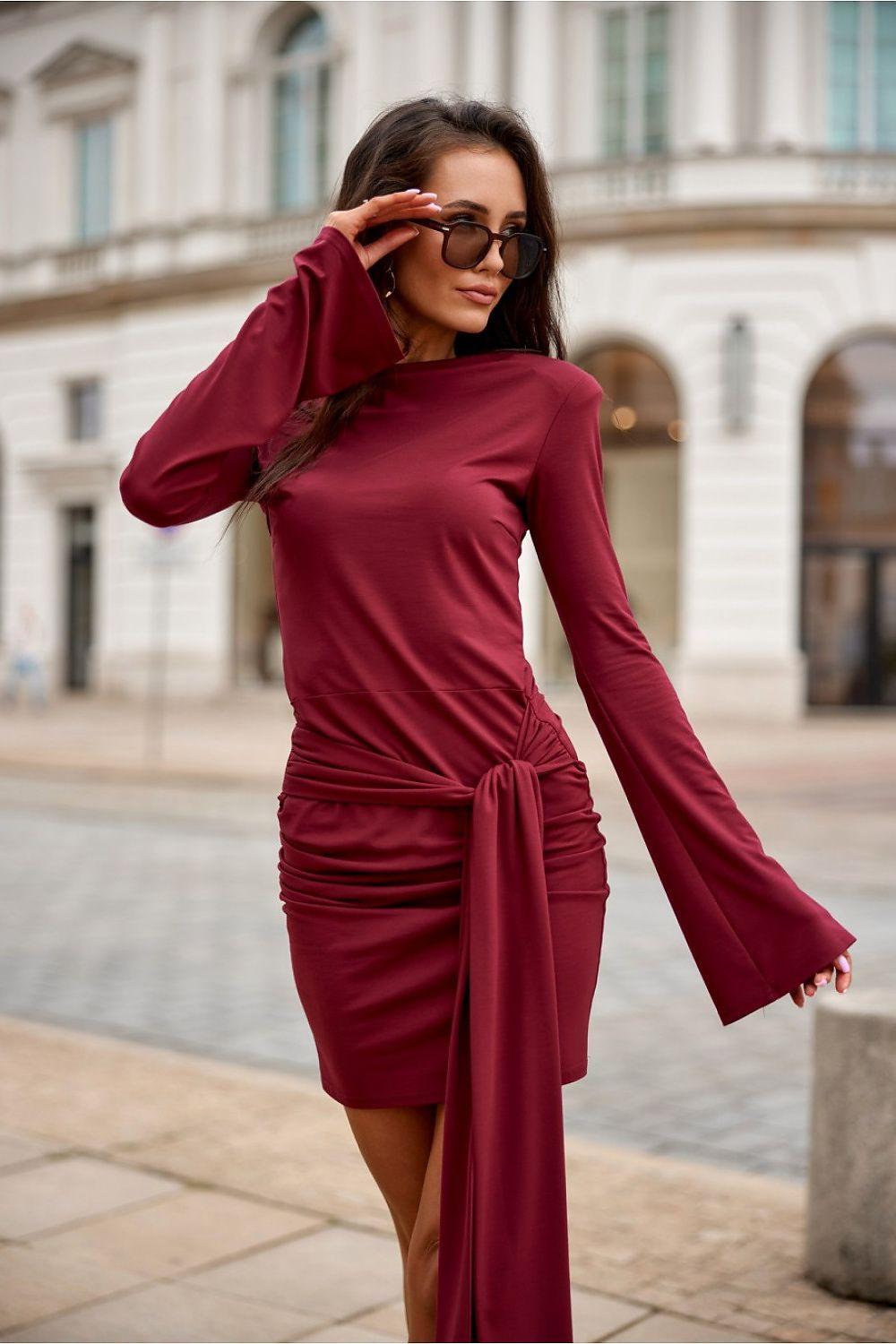 Short dark red fitted dress with long sleeves, ruched waist, draped side tie detail.