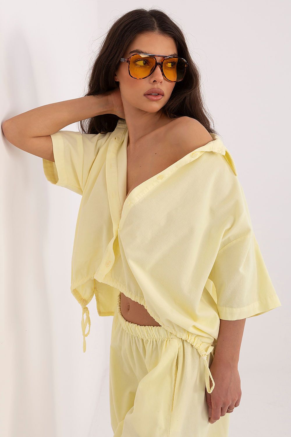 Short-sleeve button-up shirt in pale yellow with collar, loose sleeves, and side ties